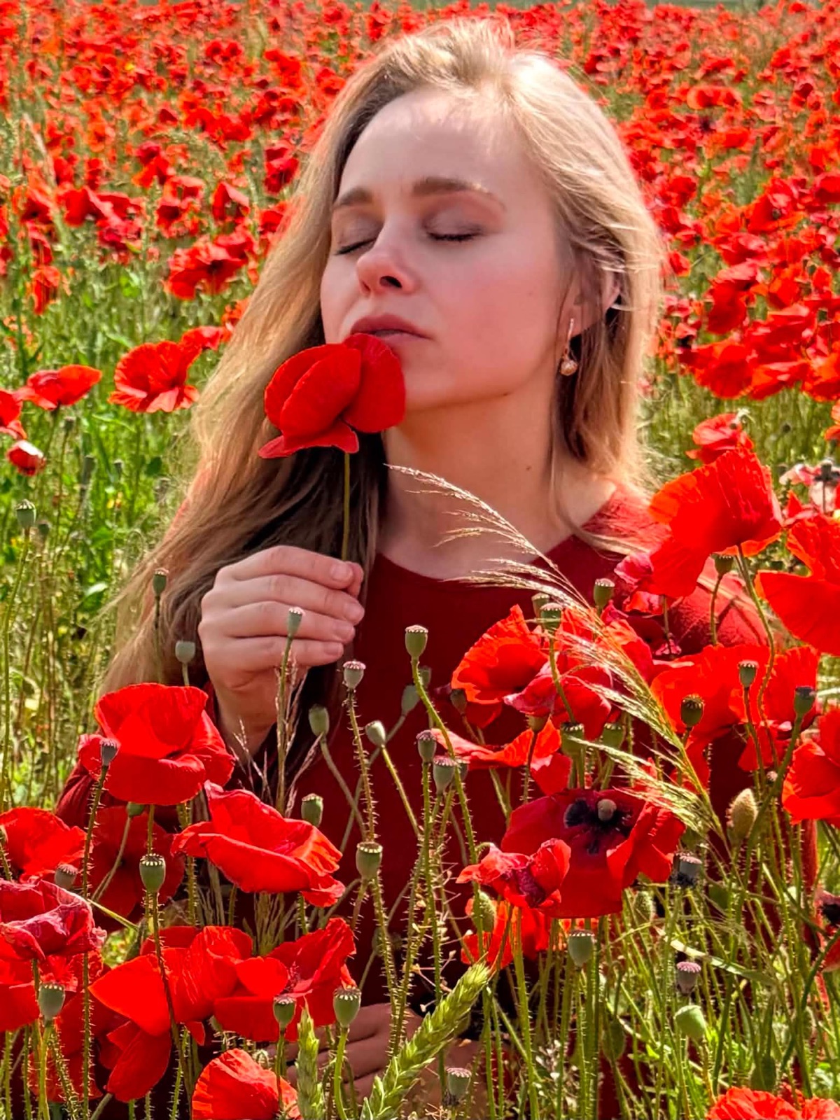 Agnė užsimerkusi laiko aguonos žiedą prie veido